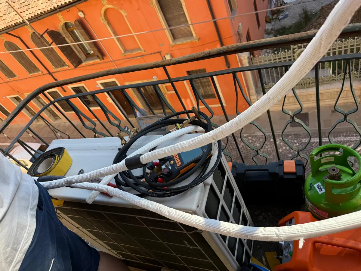 Manometro digitale collegato all'unità esterna di un condizionatore su un balcone, accanto alla bombola del gas refrigerante