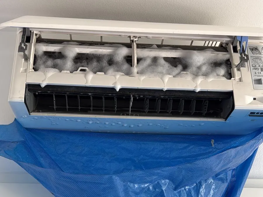 Condizionatore a parete aperto con la schiuma sanificante sulla batteria e il telo blu che protegge la parete